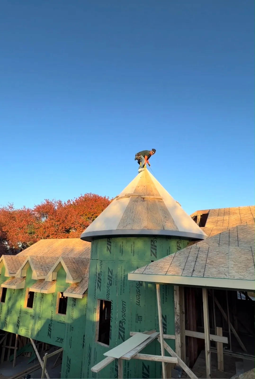 Marlon en la punta de un techo cónico, con los árboles de otoño detrás